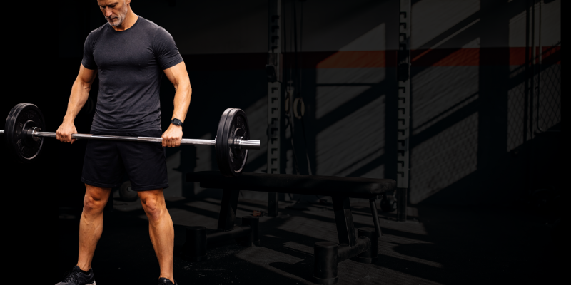 Lean middle-aged man holding full barbell in gym, focused strength training without visible abs
