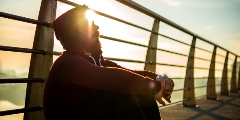 Man resting outdoors at sunrise after training, emphasizing nervous system recovery and stress regulation