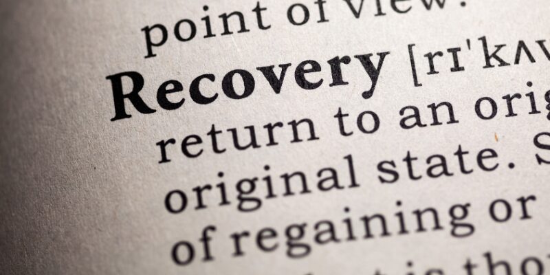 Close-up view of the word recovery in a dictionary, representing restoration and return to baseline function